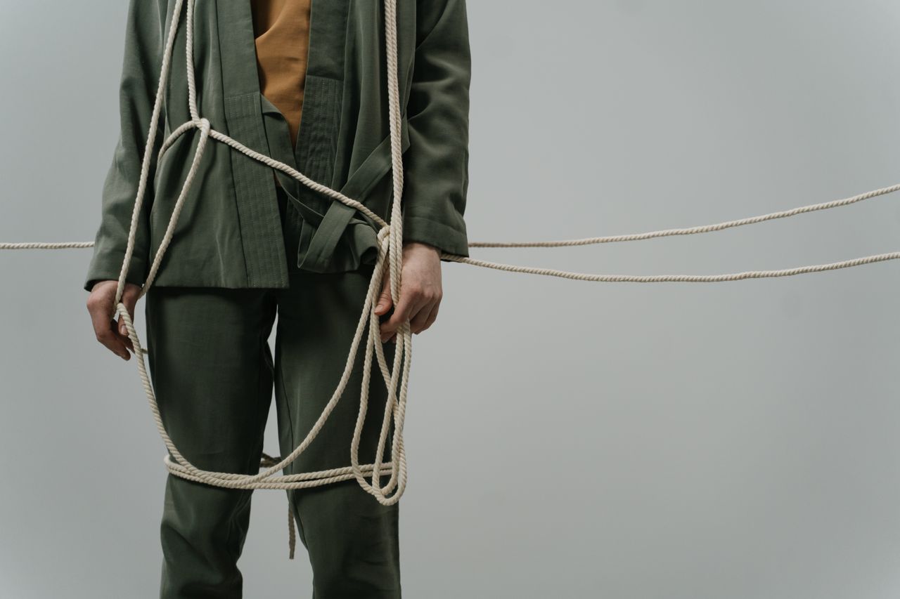 A captivating conceptual photograph showing a person in green clothes tangled with ropes, symbolizing entrapment or struggle.